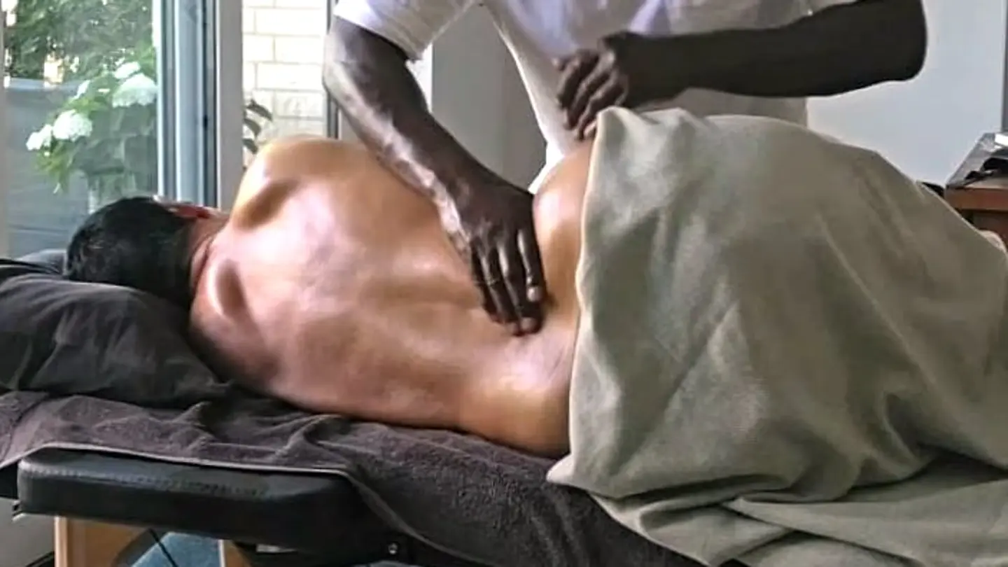 Hände arbeiten am oberen Rücken einer liegenden Person auf der mobilen Massageliege