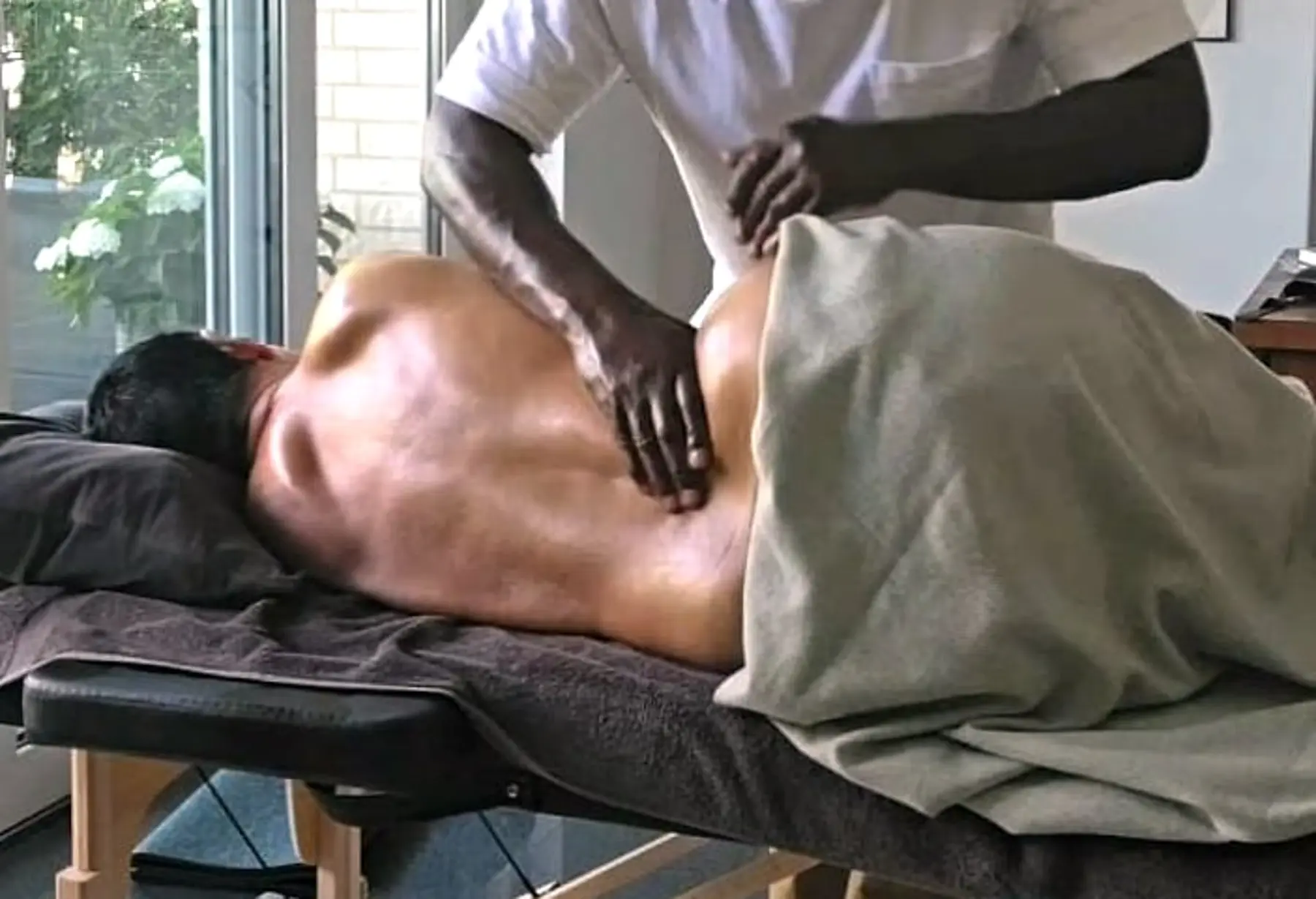 Wilfrand Brice arbeitet mit beiden Händen am oberen Rücken einer liegenden Person auf der mobilen Massageliege